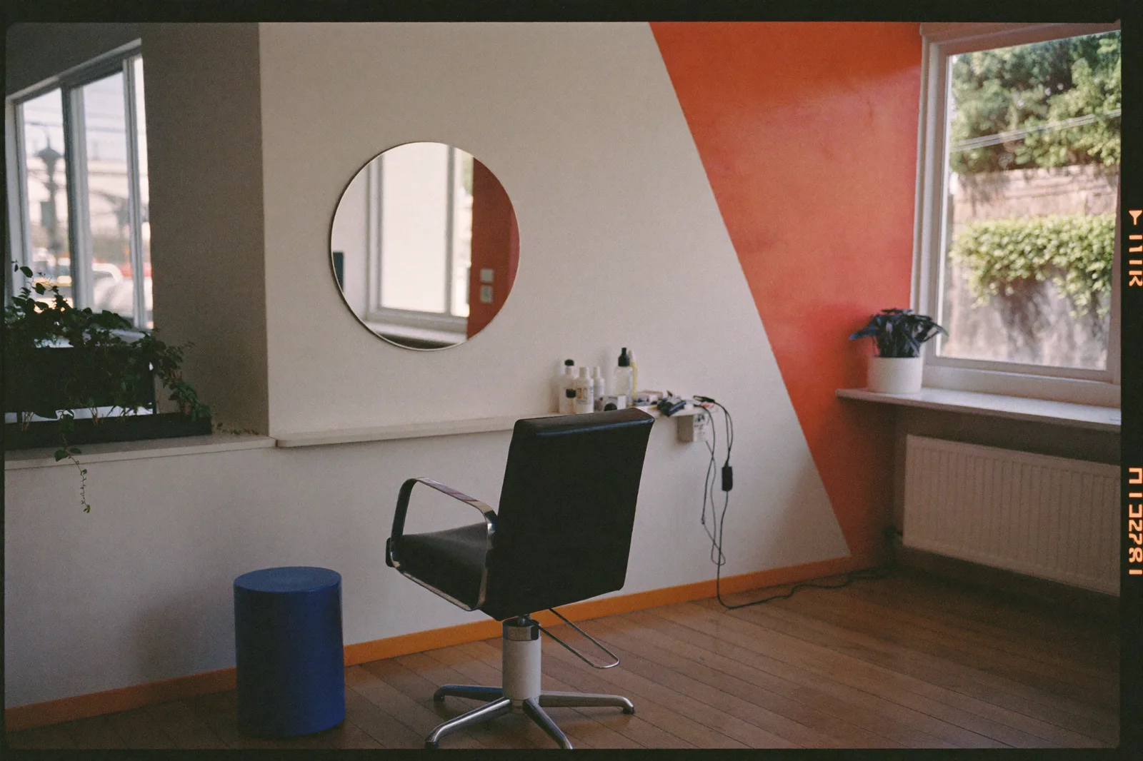 Heller Salon-Arbeitsplatz mit rundem Spiegel, Stuhl und korallenroter Wand (Symbolfoto)